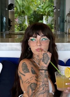 a woman with tattoos and glasses holding a drink