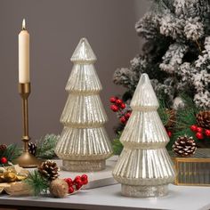 three glass christmas trees sitting on top of a table next to a candle and other decorations