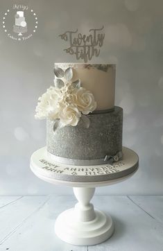 a three tiered cake with white flowers and silver lettering on top that says happy birthday