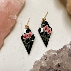 the earrings are decorated with pink flowers on black and gold earwires, sitting next to a rock