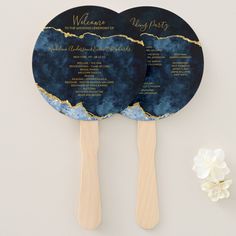 two blue and gold wedding fans with names on them sitting next to a white flower