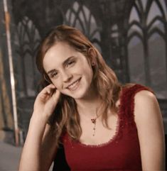 a young woman sitting at a table with her hand on her chin and smiling for the camera