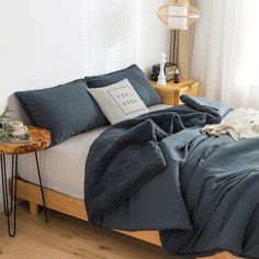 a bed with blue sheets and pillows on top of it next to a night stand