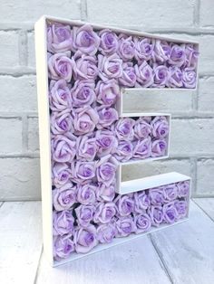 the letter e is made out of purple roses and sits in front of a brick wall