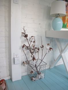 a basket with cotton flowers sitting on the floor next to a white table and lamp