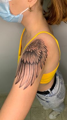 a woman with a mask on her face and an angel wing tattoo on her arm