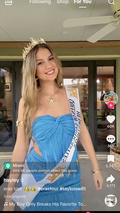 a woman in a blue dress is smiling and wearing a tiara while standing next to a building