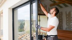 a man in white shirt and black gloves working on sliding glass door with rollers