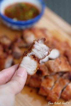 a person is holding up some food on a cutting board with dipping sauce in the background