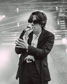 a man in a suit and sunglasses holding a microphone up to his mouth while standing on stage