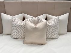 four pillows on a bed with white sheets and tan headboard, all lined up