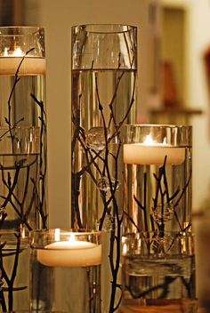 candles are lit in glass vases with branches