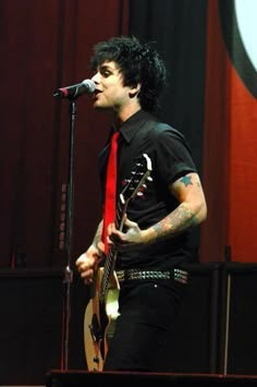 a man with black hair and tattoos on his face singing into a microphone while wearing a red tie