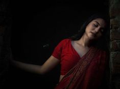 a woman with her eyes closed standing in front of a brick wall and wearing a red sari