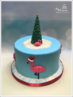 a blue cake decorated with a pink flamingo and a christmas tree