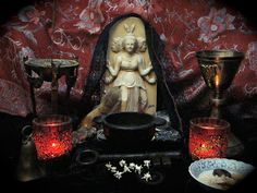 an assortment of decorative items displayed in front of a red wallpapered background, including a statue and candles