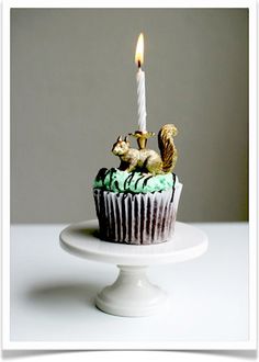 a cupcake with a squirrel figurine on top and a candle in the middle