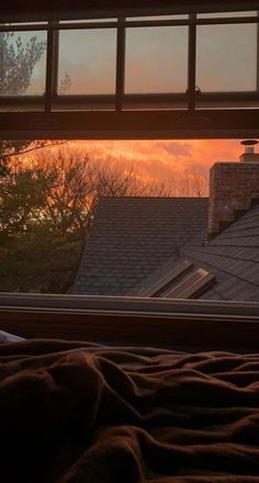 the sun is setting in front of a window with a view of rooftops and trees