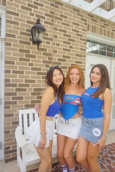 three young women standing next to each other in front of a brick wall and white bench