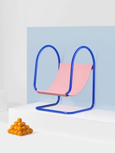 a pink and blue chair sitting on top of a white table next to oranges