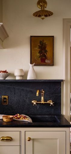 a kitchen sink with gold faucet and black counter top next to a painting on the wall