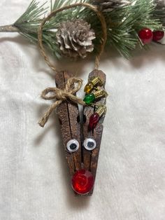 an ornament made out of wooden sticks with eyes and bells on it, hanging from a pine tree branch