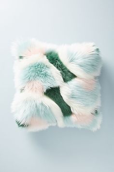 a green and white fur pillow sitting on top of a gray wall next to a plant