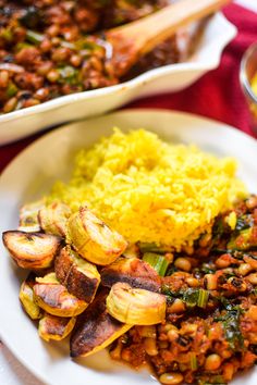 a white plate topped with lots of food next to a bowl filled with rice and beans