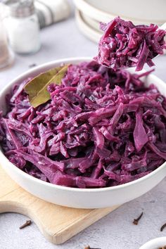 a white bowl filled with red cabbage on top of a wooden cutting board