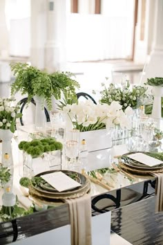 the table is set with white flowers and greenery in glass vases on each side