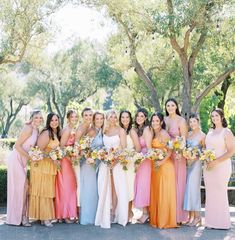 a group of women standing next to each other wearing dresses and holding bouquets in their hands