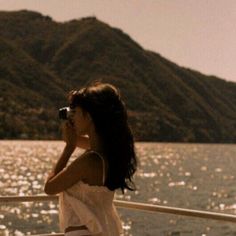 a woman on a boat looking out over the water with mountains in the background,