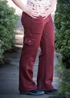 a woman in red pants standing on a sidewalk with her hands on her hips and looking at the camera