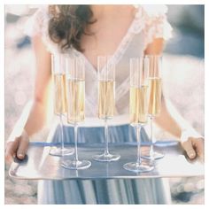 a woman holding a tray with champagne glasses on it and three wine glasses in the middle