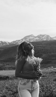 black and white photograph of a woman holding flowers in front of the mountains with snow capped peaks behind her