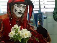 a man dressed as a clown with flowers in front of him and another person behind him