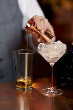 a bartender pouring a drink into a glass with ice cubes on the table next to it