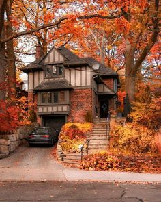 a car parked in front of a house surrounded by trees with orange leaves on the ground