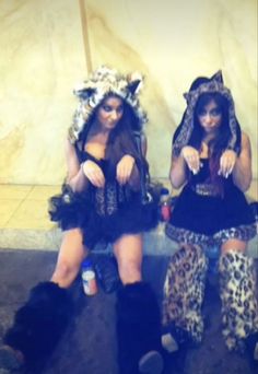 two women dressed in animal print outfits sitting on the ground with their legs crossed and one holding a cell phone