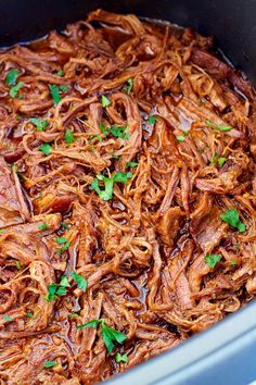 shredded pulled pork in a slow cooker with parsley garnish on top