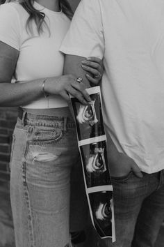 a man and woman standing next to each other in front of a brick wall with their arms around each other