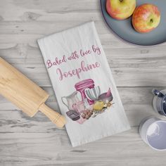 a tea towel that says bake with love by jesperpine next to two apples