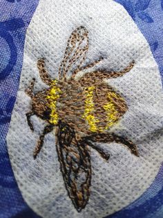 a close up of a bee on a blue and white cloth with gold thread work