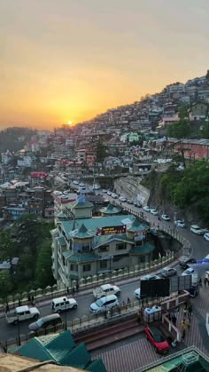 the sun is setting over a city with lots of cars parked on the side of the road