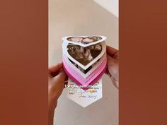 someone is holding up an origami heart shaped box with two photos inside it