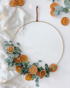 orange slices and eucalyptus leaves are arranged in a circle on a white surface with string lights