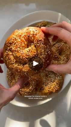 two hands reaching for a bagel on a white plate with sesame seed sprinkles