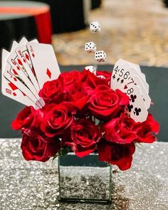 a vase filled with red roses and cards sitting on top of a table next to dice