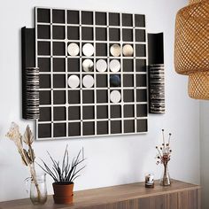 a table with vases and plants on it in front of a wall mounted art piece