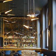 an empty bar with blue chairs and lights hanging from the ceiling in front of it